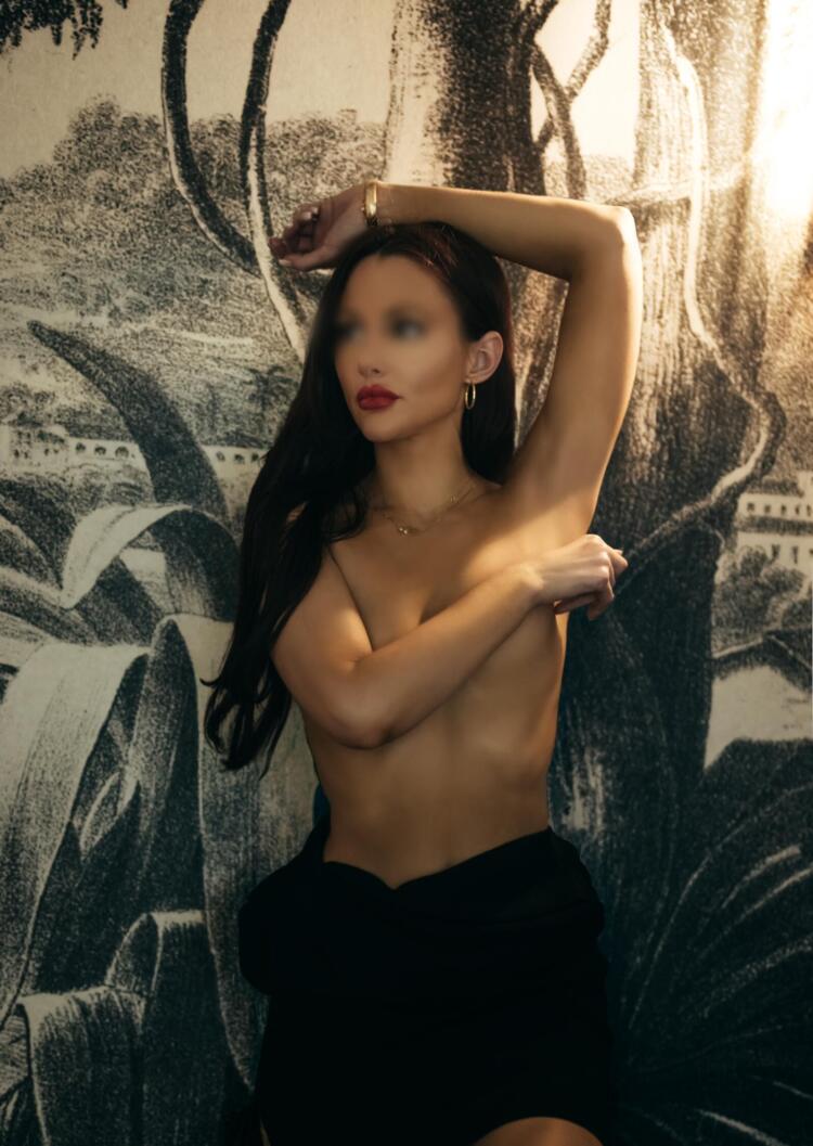 Toronto escort with long brunette hair poses for the camera in front of a jungle theme in a barely there black dress